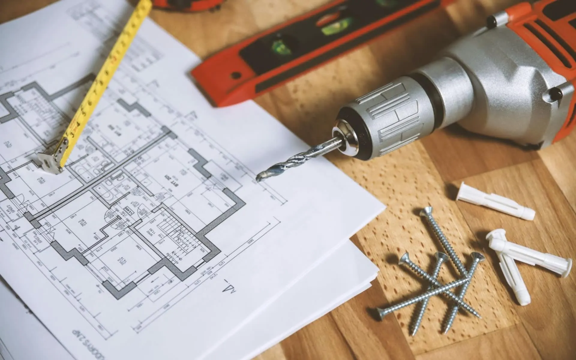 A power drill and blueprints on a wooden table.