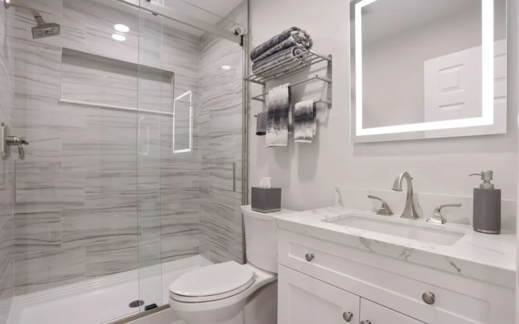 Modern bathroom with white marble tiles and glass shower door.