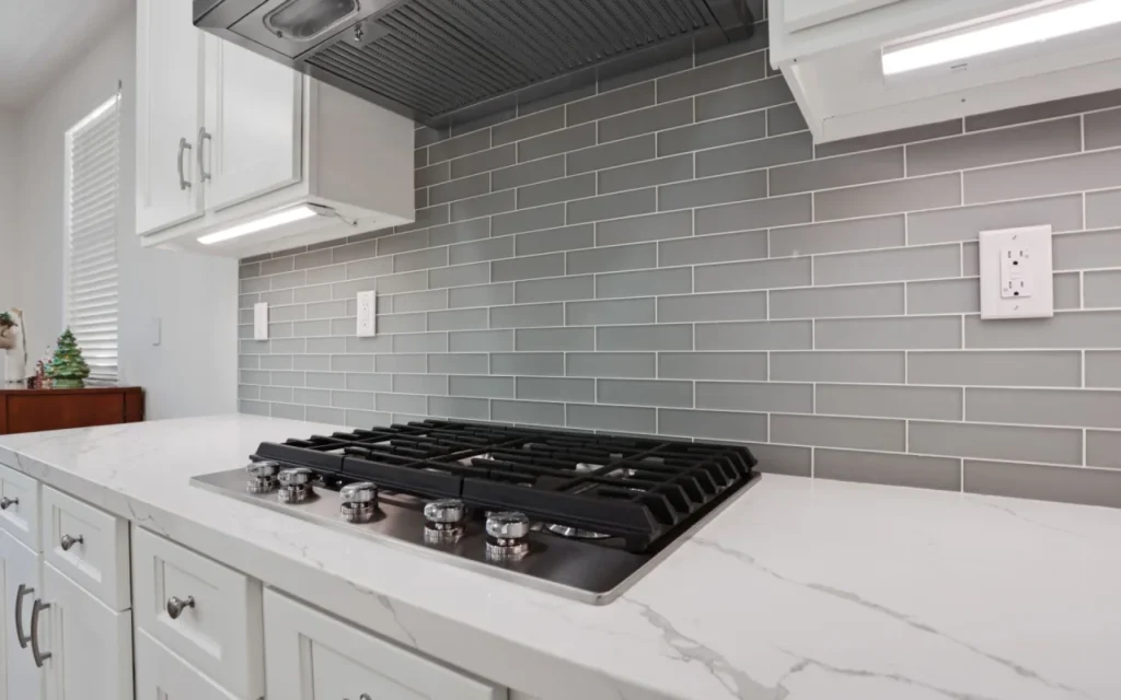 A gas stovetop with a gray tile backsplash.