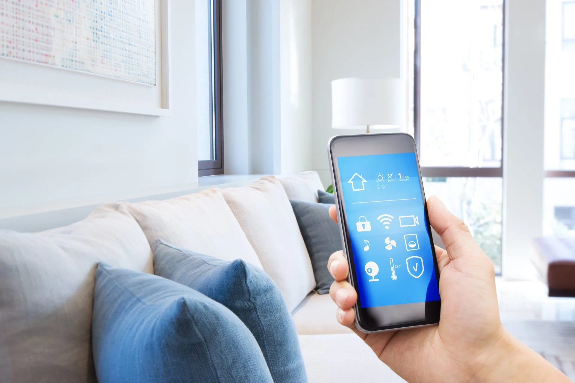 A hand holding a smartphone with a smart home app on the screen.