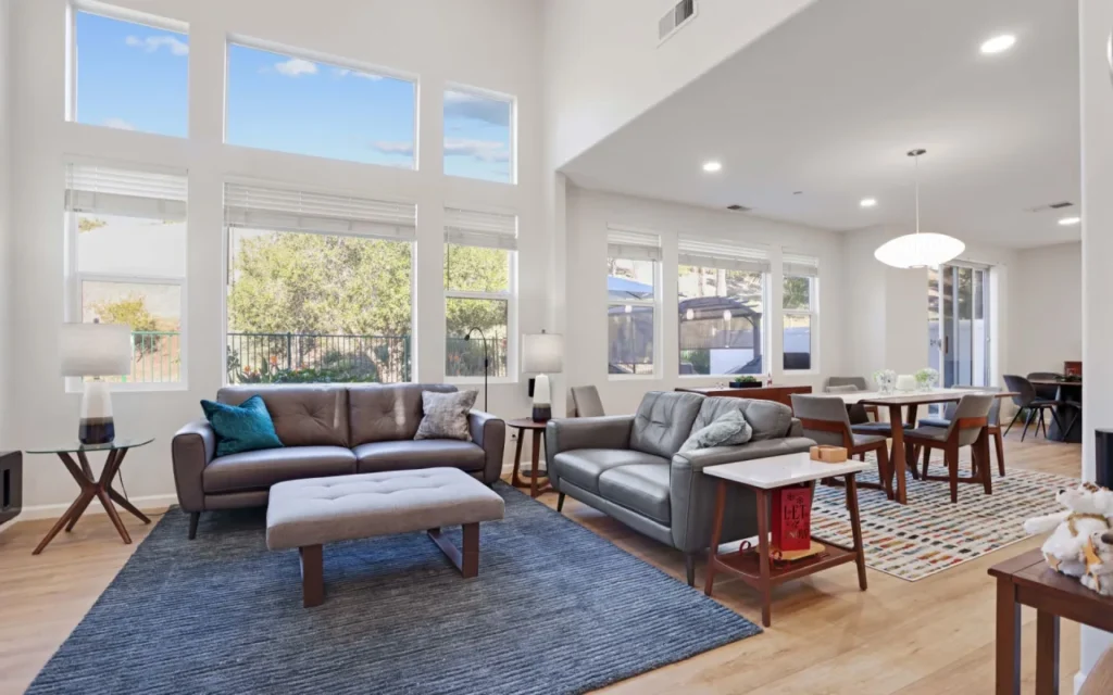 A living room with a sofa, rug, coffee table, and dining table in the background.