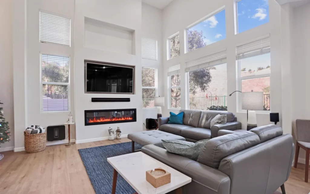 A living room with a fireplace, TV, couch, rug, and windows.