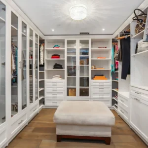 An organized walk-in closet with white cabinets and a crystal chandelier.