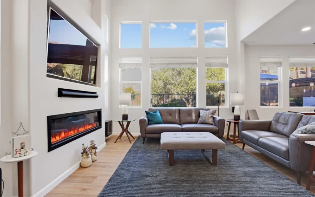 A living room with a fireplace, TV, and large windows.
