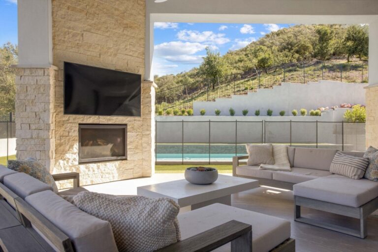 Outdoor living space with fireplace, TV, and pool.