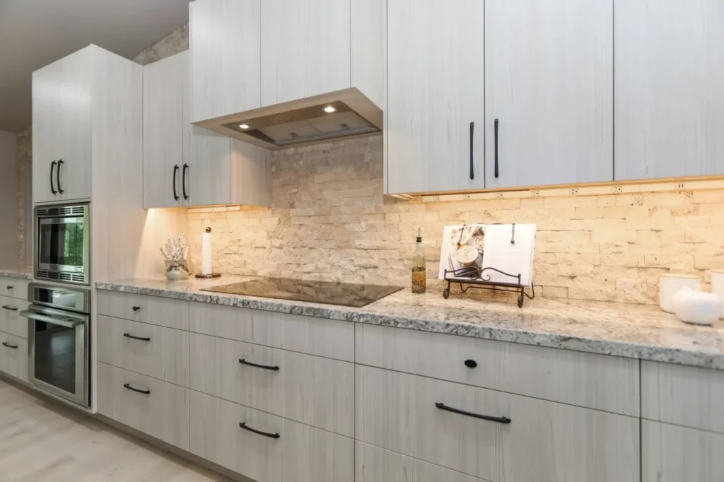 A modern kitchen with white cabinets and a stone backsplash.