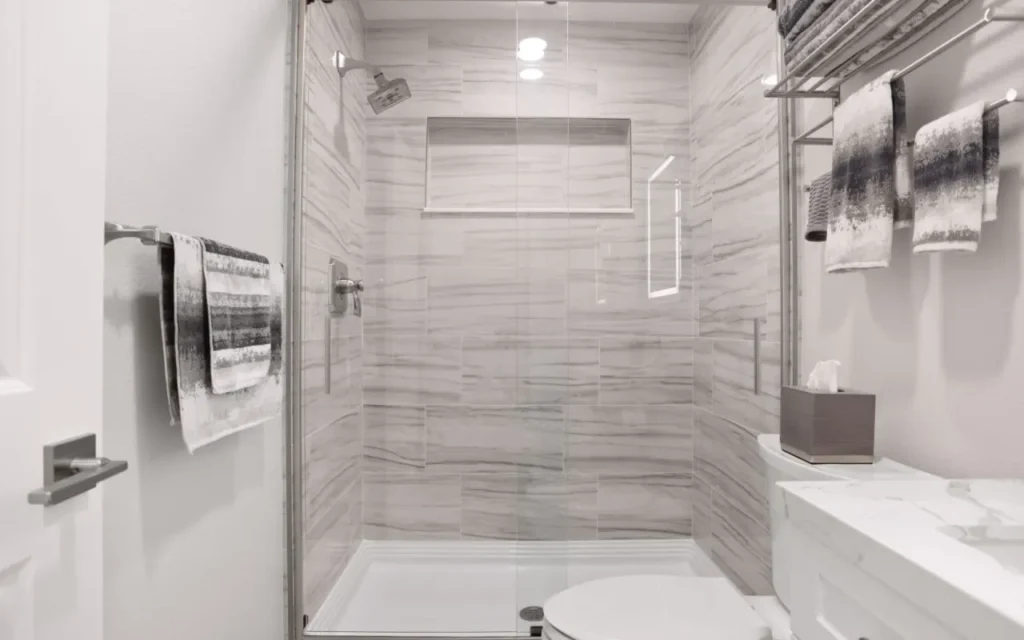Modern bathroom with white marble tiles and glass shower door.