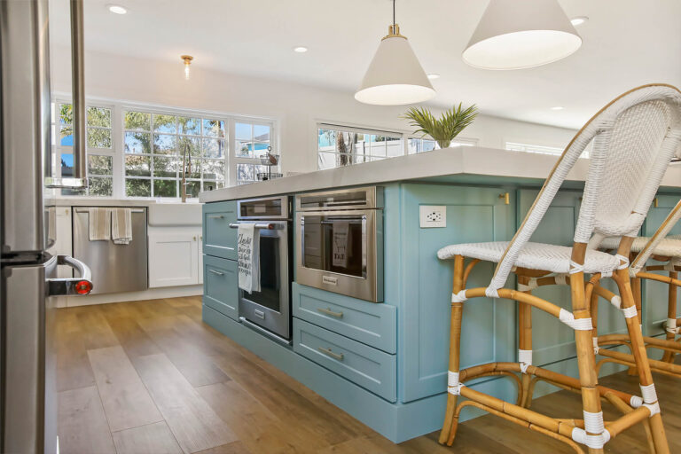 Blue kitchen island with white marble top and wicker bar stools.