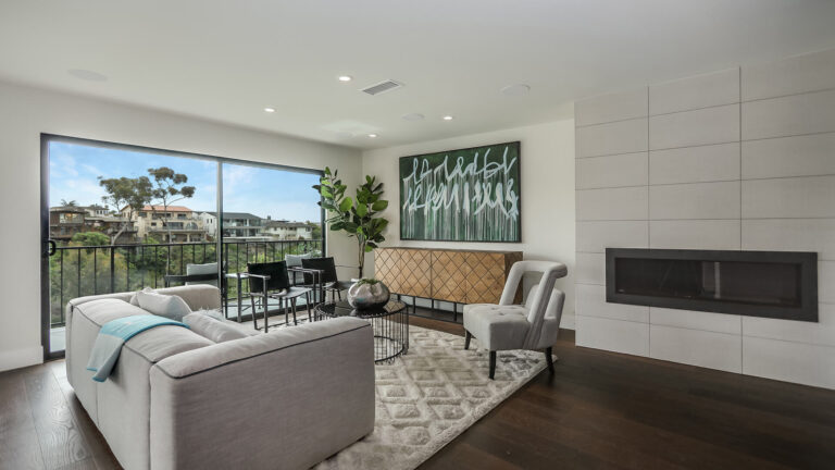 A living room with a fireplace, sofa, rug, coffee table, two chairs, and a balcony with a view.